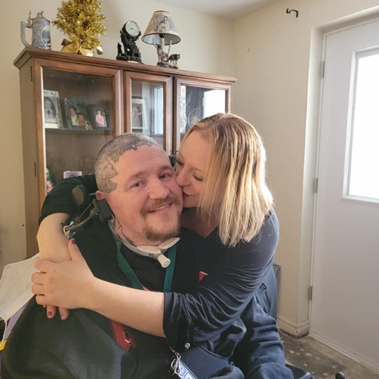 Man in wheel chair being hugged and kissed by a woman