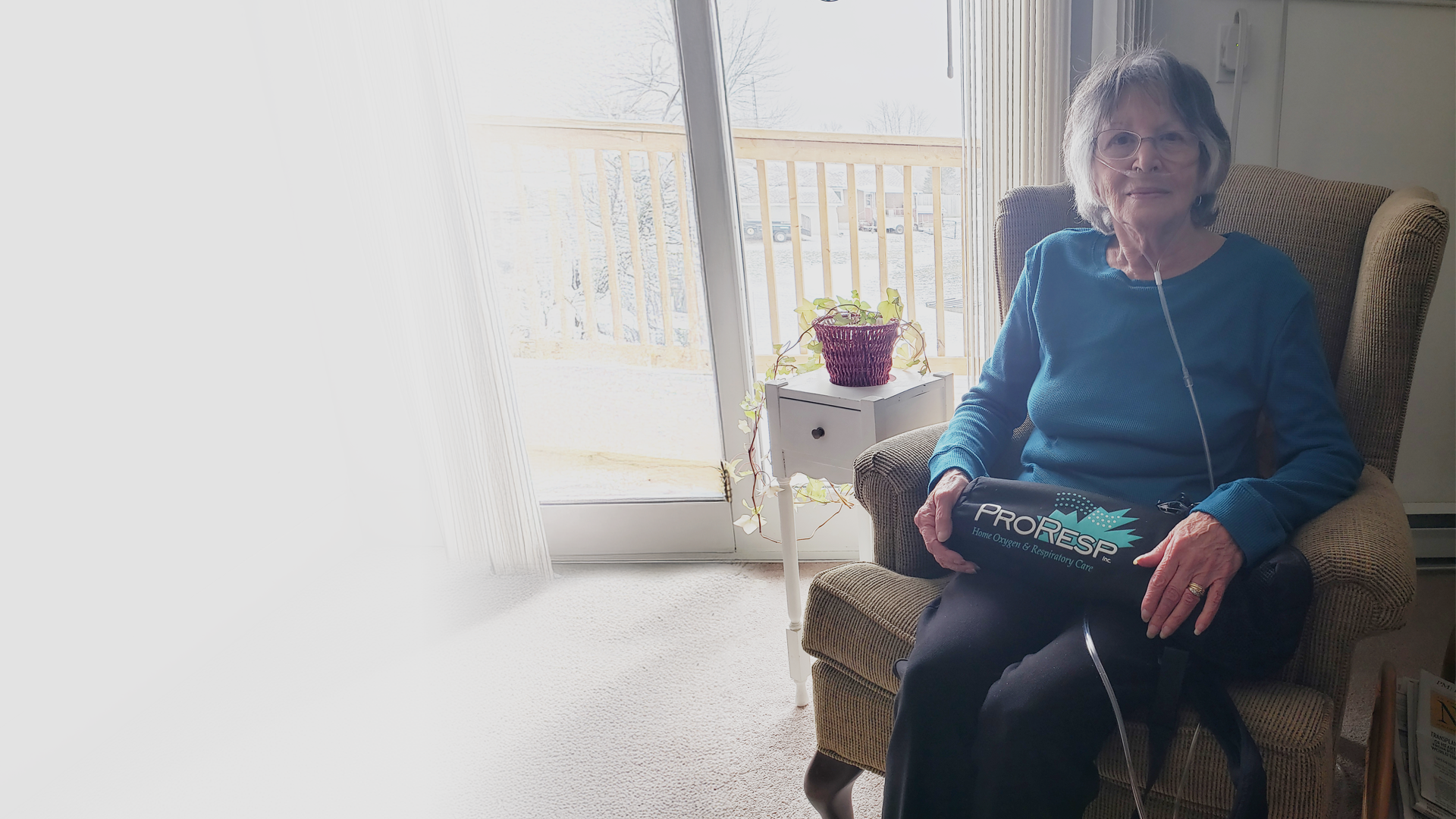 woman sitting in chair with oxygen cylinder on lap and wearing a nasal cannula